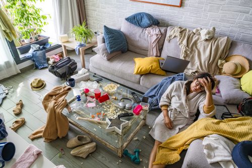 Tired woman in bathrobe, eyes closed sitting on the floor of a messy living room. High resolution 42Mp indoors digital capture taken with SONY A7rII and Zeiss Batis 25mm F2.0 lens